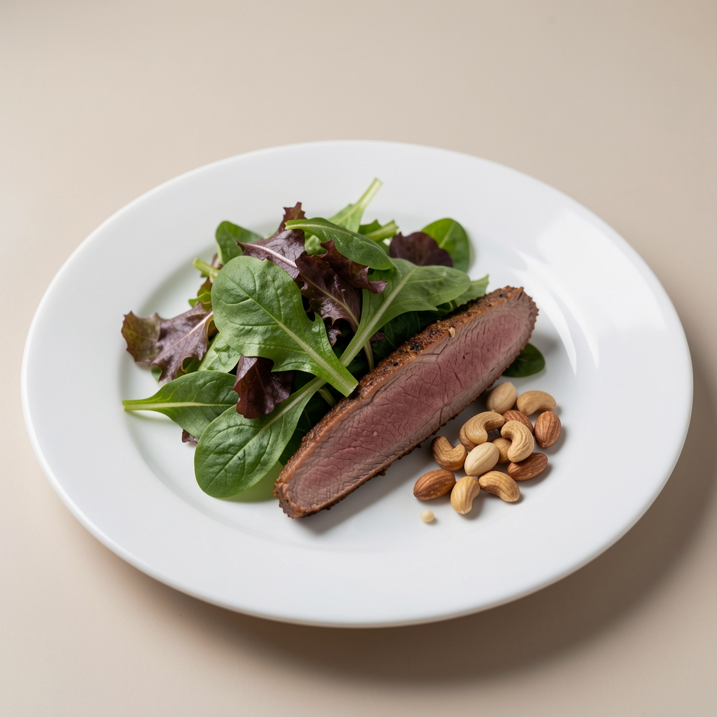 A measured portion of salad greens, lean protein, and a small handful of nuts on a plain white plate against a neutral background